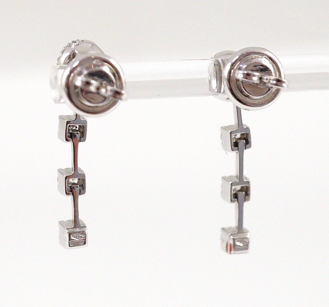 A modern pair of 18ct white gold, diamond cluster and three stone diamond drop set earrings